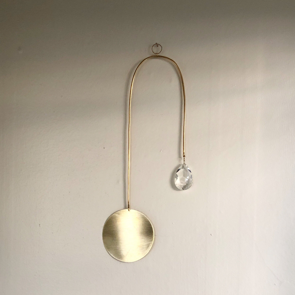 Golden Hour Suncatcher featuring hand forged brass wire and vintage glass crystal, displayed on wall