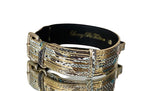 Gold-tone pet collar with intricate hammered texture and black inner lining, displayed on a reflective surface.