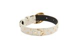 White leather bracelet with gold polka dots and gold oval buckle hardware, displayed on a white background with the inner side of black leather visible.