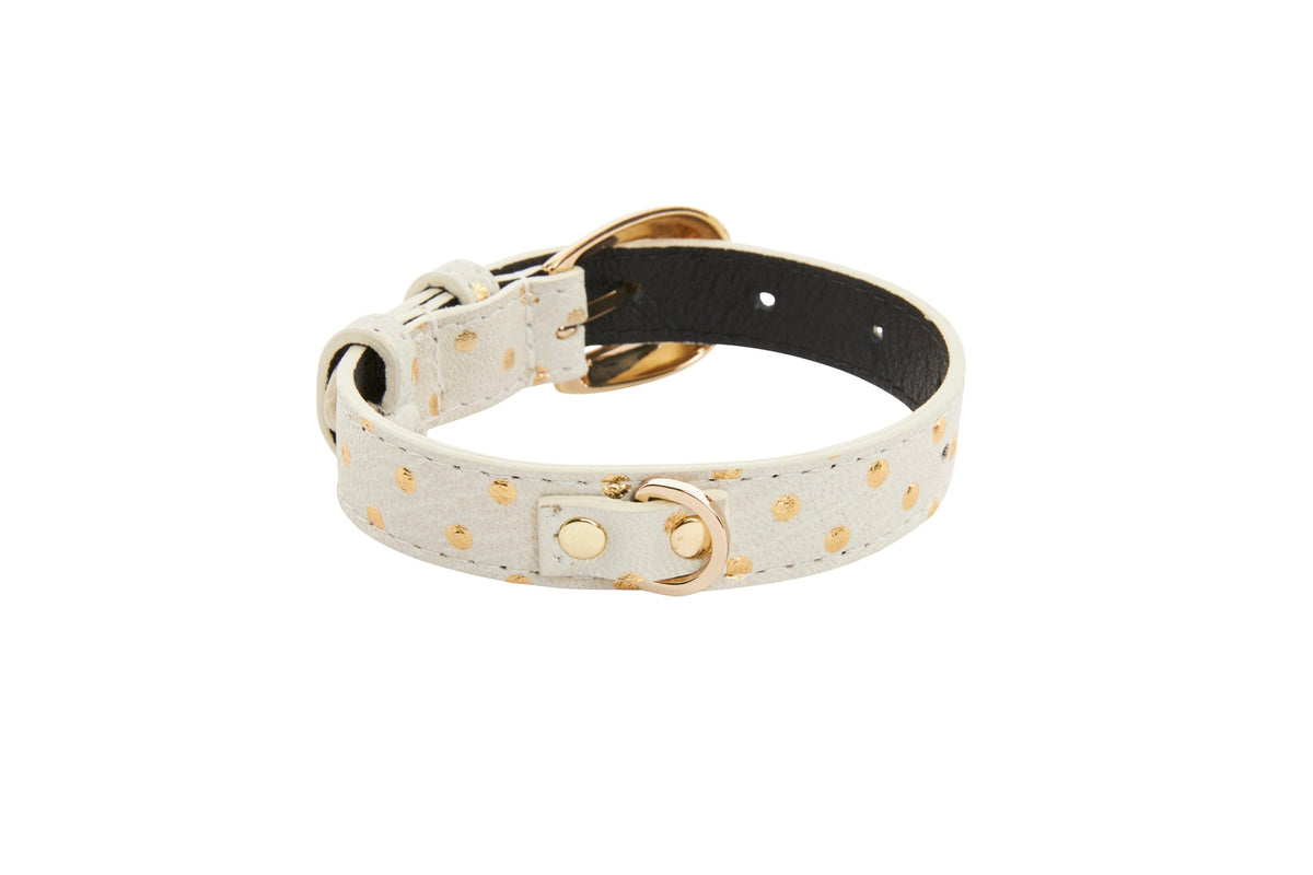 White leather bracelet with gold polka dots and gold oval buckle hardware, displayed on a white background with the inner side of black leather visible.