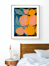 Framed botanical art print above bed featuring overlapping orange and peach citrus shapes with layered blue-green leaves against a black background.