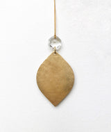 Leaf-shaped golden pendant with a hammered texture, hanging from a thin gold cord with a faceted clear glass crystal bead above it.