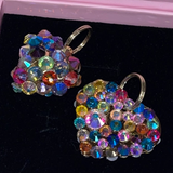 Pair of heart-shaped earrings encrusted with multicolored Swarovski crystals in various sizes, displayed on black velvet with silver hoop attachments.