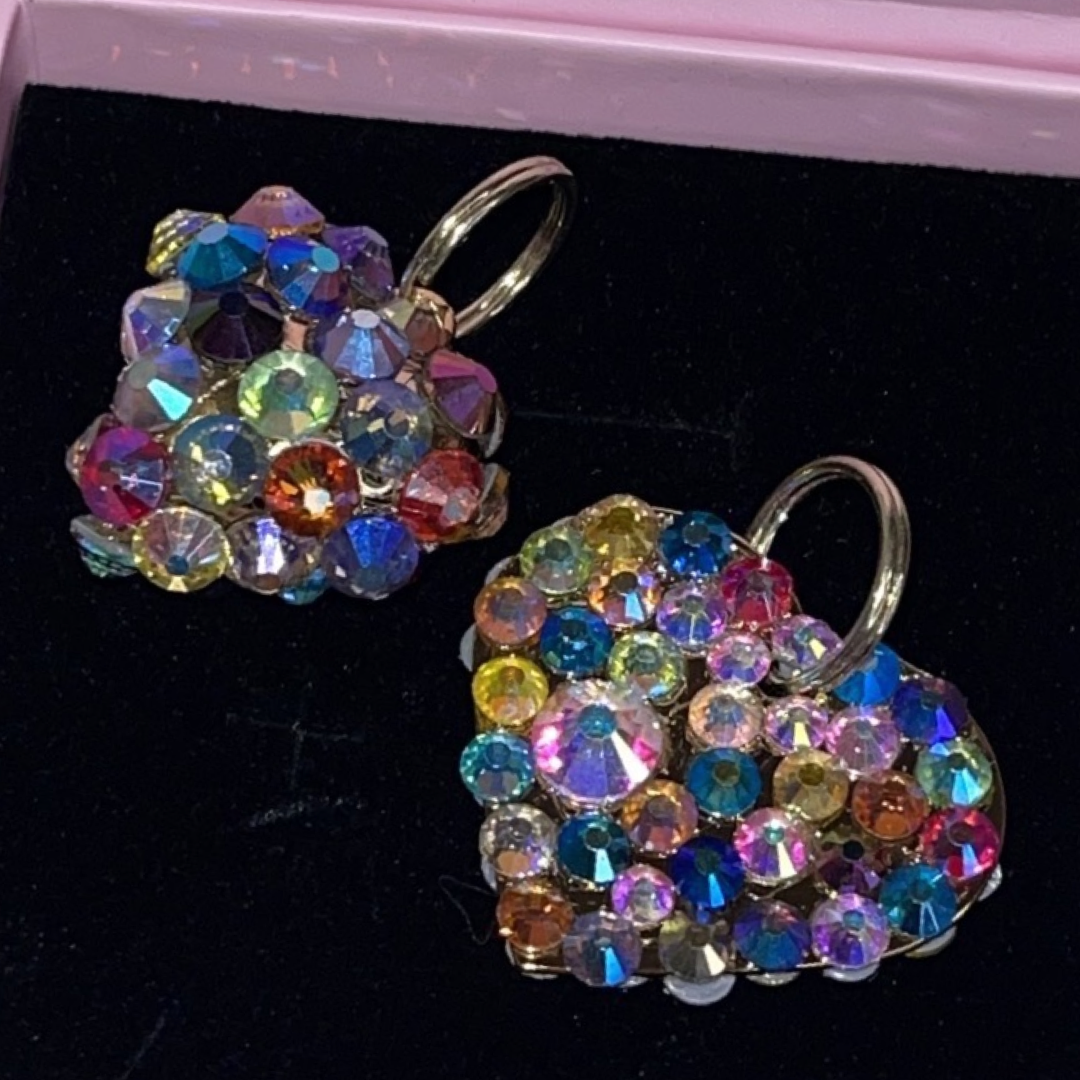 Pair of heart-shaped earrings encrusted with multicolored Swarovski crystals in various sizes, displayed on black velvet with silver hoop attachments.