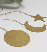 Three flat brass ornaments shaped as a circle, crescent moon, and star, each with a small loop and cord for hanging, shown on a white surface.