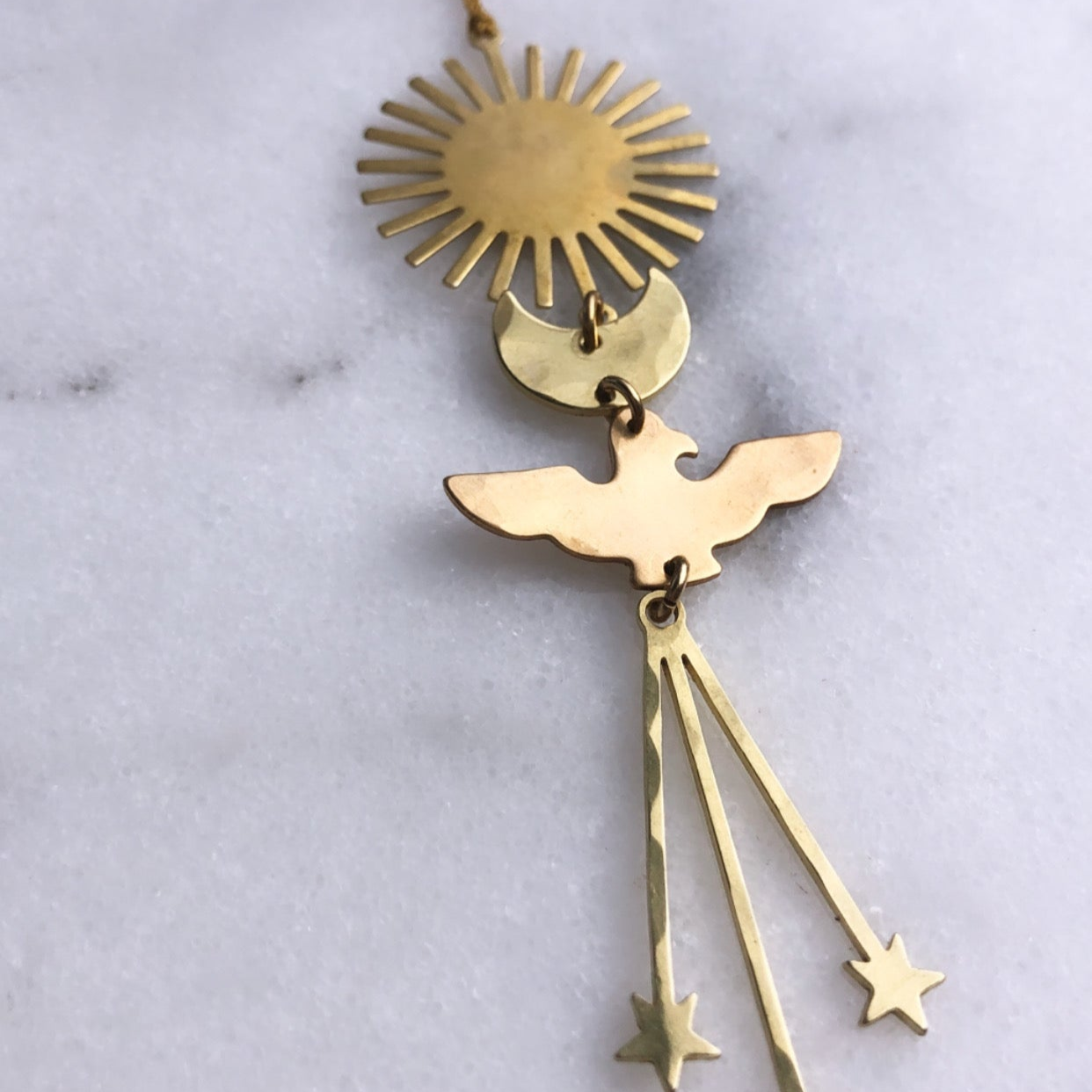 Keeper of the Stars Ornament by Vida + Luz hanging against a black background showing its brass metal texture
