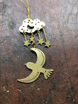 Brass ornament featuring a cloud with three dangling stars above a bird with engraved feather details, all suspended on a dark textured surface.