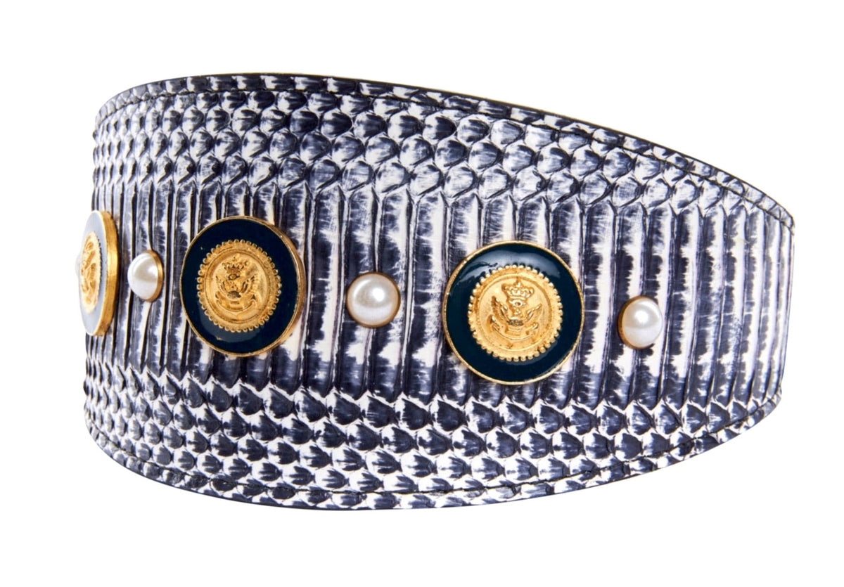 Curved bracelet with white and navy snake-patterned texture, decorated with alternating gold nautical emblem buttons and small white pearls.