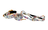 White leather collar, leash, and harness set featuring a colorful floral mosaic pattern with gold-tone hardware and Swarovski crystal accents, displayed on a white background.