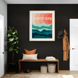 Framed modern art print with abstract layered waves in teal blues, coral, and peach hues titled 'Siesta Key Florida' hanging on a dark wall above a wooden bench with pillows.