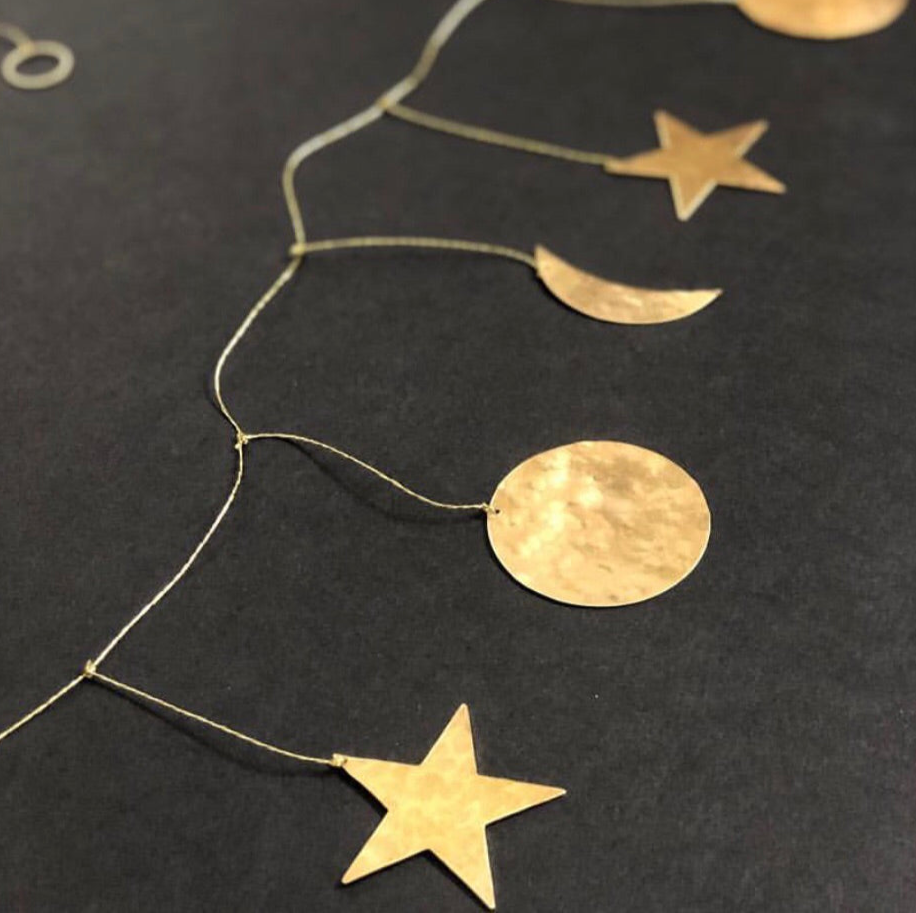 Galaxy Hammered Brass Garland by Vida + Luz, hand-cut and hammered brass sheets strung in a decorative wall hanging