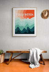 Framed Folly Beach South Carolina art print with abstract layered waves in shades of blue and orange, hanging above a wooden bench with a white blanket and a hat on the wall.