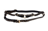 Black leather harness with gold polka dots and gold hardware buckles laid flat on a white background.