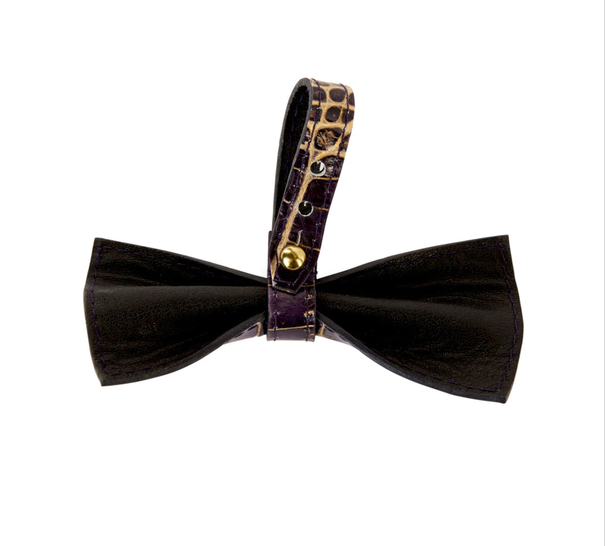 Bow tie made of dark purple leather with a gold crocodile-embossed leather strap featuring a gold button closure.