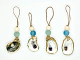 Four sea glass and shell ornaments with beige beads and jute hanging loops, featuring shells edged with gold and varying natural shell interiors.