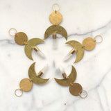Five brass moon-shaped ornaments with hammered round discs and clear quartz crystal pendants arranged in a star pattern on a white marble surface.