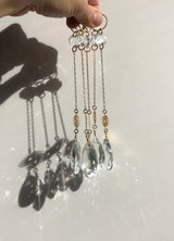 Four hanging sun catchers with gold chains, small clear crystal beads near the top, and larger faceted clear glass crystals at the bottom casting intricate shadows on a white surface.