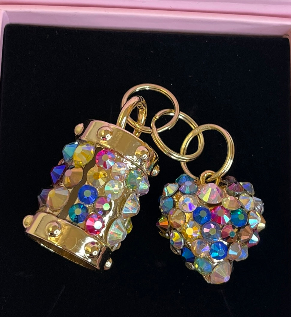 Set of two gold-tone charms with multicolored Swarovski crystals, one heart-shaped and one cylinder-shaped, displayed on a black velvet background.