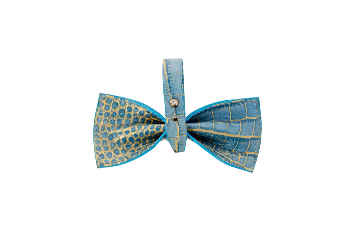 Blue leather bow tie embossed with a crocodile pattern featuring gold accents and a central strap embellished with a small decorative gem.