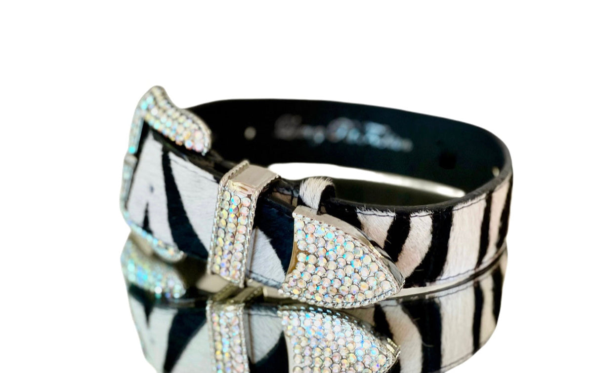 Italian leather pet collar with tiger print hair-on-hide pattern, featuring a buckle and bow-shaped hardware encrusted with Swarovski crystals, shown on a reflective surface.