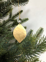 Gold leaf-shaped Christmas ornament hanging from an evergreen branch, topped with a clear vintage glass crystal bead and suspended on a gold thread.