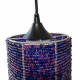 Pendant light shade woven from small blue and purple beads forming a cylindrical shape, suspended by a black cord and black metal frame.