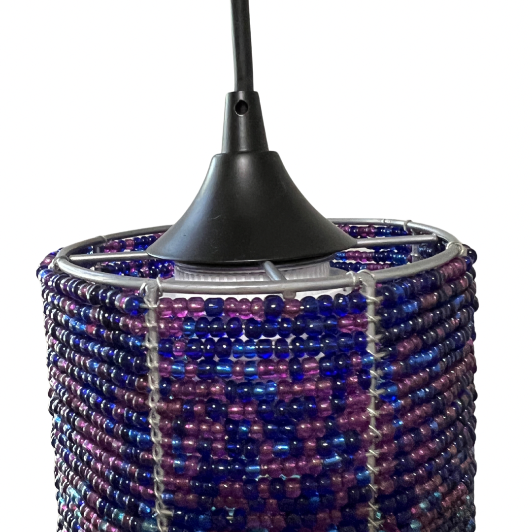 Pendant light shade woven from small blue and purple beads forming a cylindrical shape, suspended by a black cord and black metal frame.