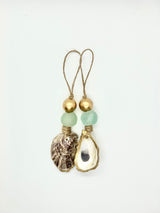Two hanging ornaments each with a golden bead, a matte green sea glass piece, and a natural seashell wrapped in gold-toned wire or twine, looped at the top.