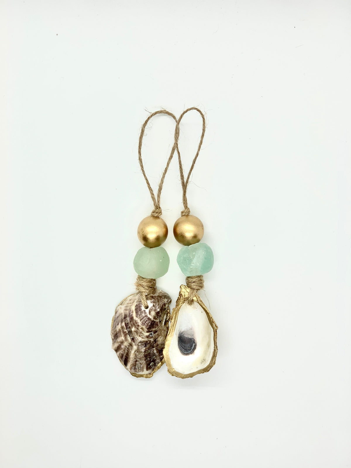 Two hanging ornaments each with a golden bead, a matte green sea glass piece, and a natural seashell wrapped in gold-toned wire or twine, looped at the top.