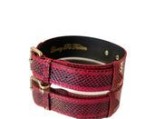 Red and black viper snake pattern dog collar with gold-toned classic buckle hardware, shown slightly angled on a reflective white surface.