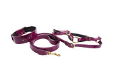 Set of purple patent leather collar, leash, and harness with gold metal hardware, shown on a white background in a loose arrangement.