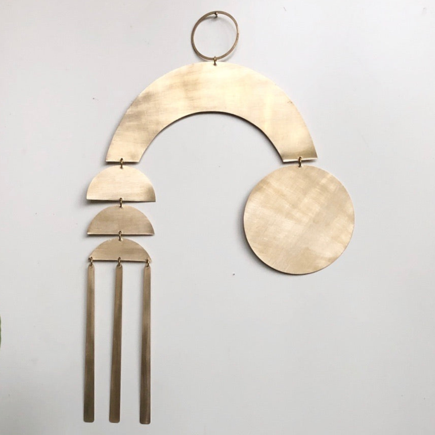 Dream Weaver brass wall hanging by Vida + Luz, hand-cut brass shapes arranged in an abstract vertical design.