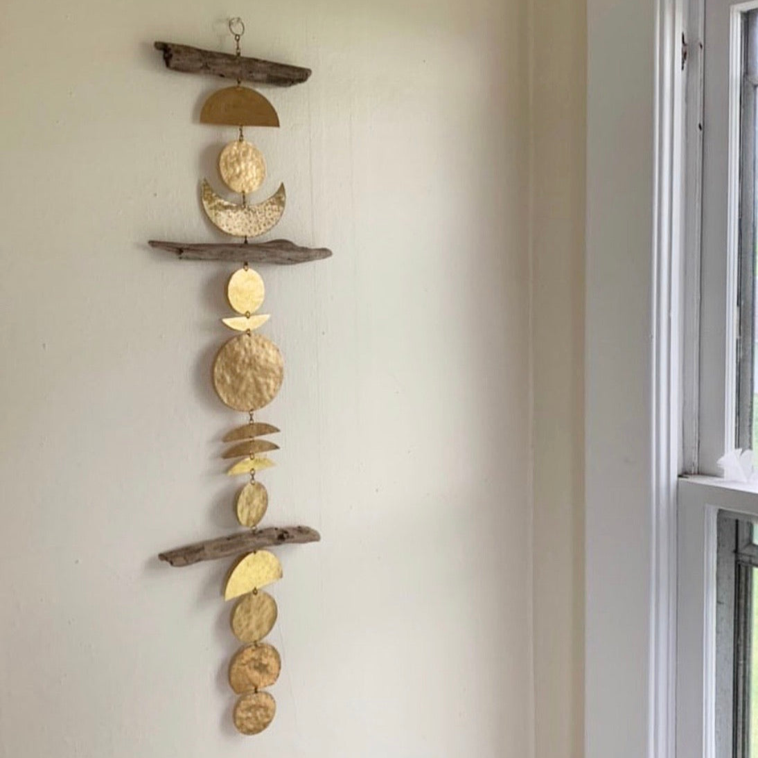 Turning of the Tides wall hanging made of driftwood and hammered brass, hanging on white wall