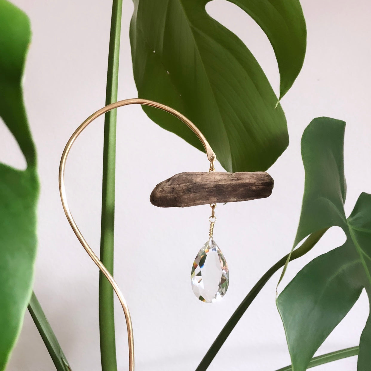 Planty Suncatcher Stick composed of driftwood and brass wire holding a vintage glass crystal catching sunlight
