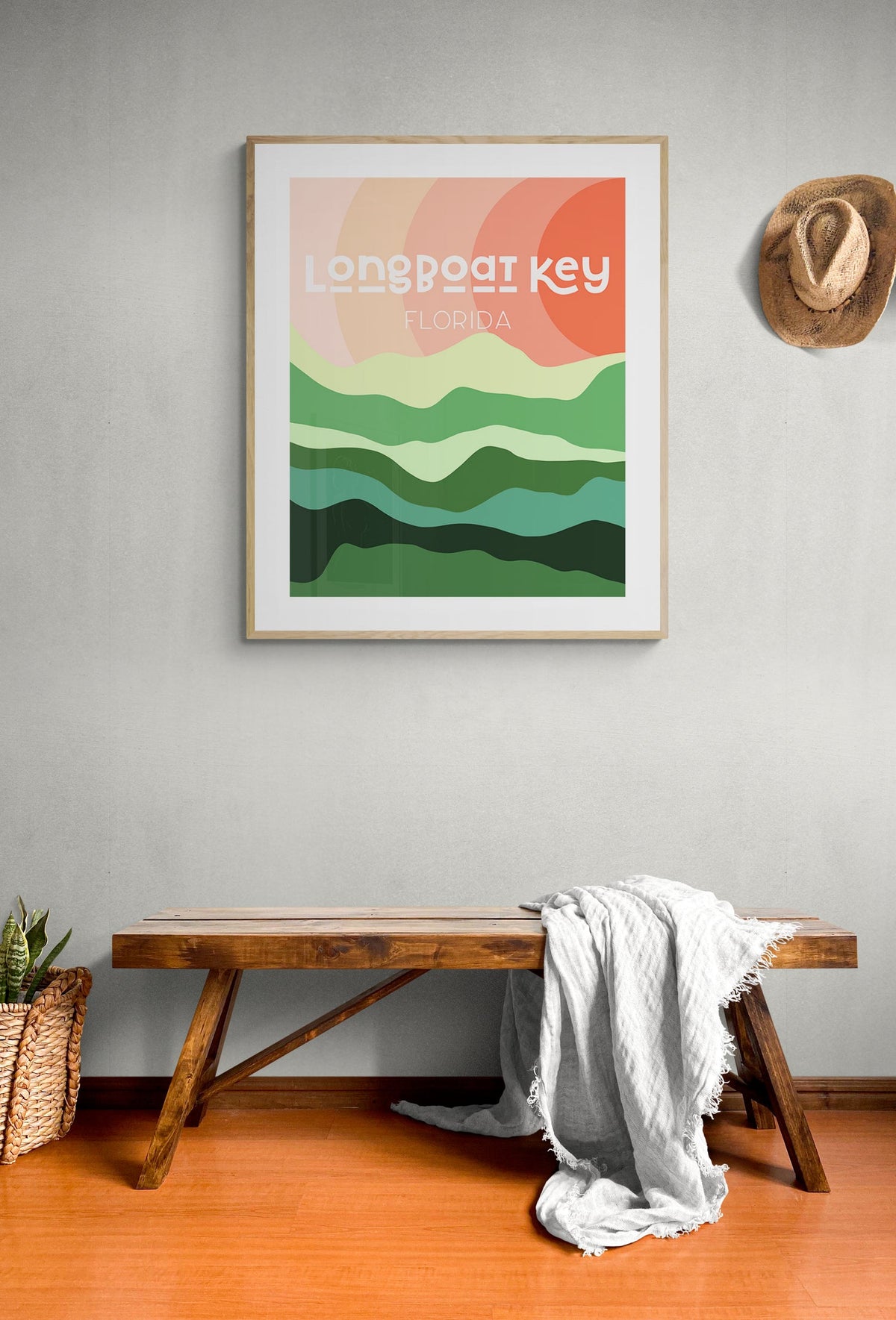 Framed Longboat Key, Florida print with layered green hills under a peach and coral sunset, hanging above a rustic wooden bench with a draped white cloth.