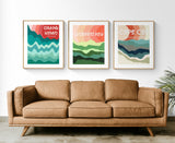 Three framed abstract landscape prints above a tan leather sofa, each with layered waves in blue, green, and red hues and location names: Grand Haven, Longboat Key, Cape Cod.