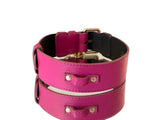 Soft fuchsia leather pet collar with gold-tone hardware and rivet accents on textured surface, shown from side angle.