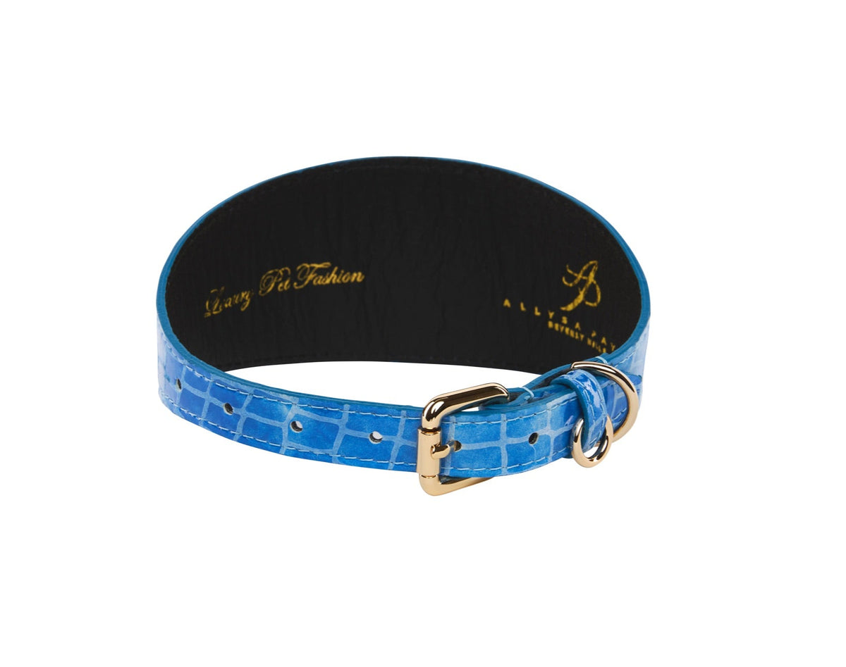 Blue patent leather dog collar embossed with a crocodile pattern, featuring a gold-tone buckle and loop, shown in a circular arrangement on white background.