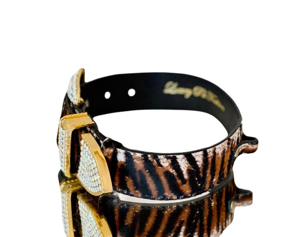 Tiger print hair-on-hide leather pet collar with gold buckle encrusted with clear Swarovski crystals, shown on reflective black surface.