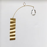Metal suncatcher with a wavy gold rectangular strip on one end and a clear faceted teardrop crystal suspended on the other, hanging against a white background.