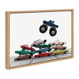Framed canvas showing a blue monster truck hovering above a colorful pyramid stack of vintage toy cars on a wooden floor with white background.