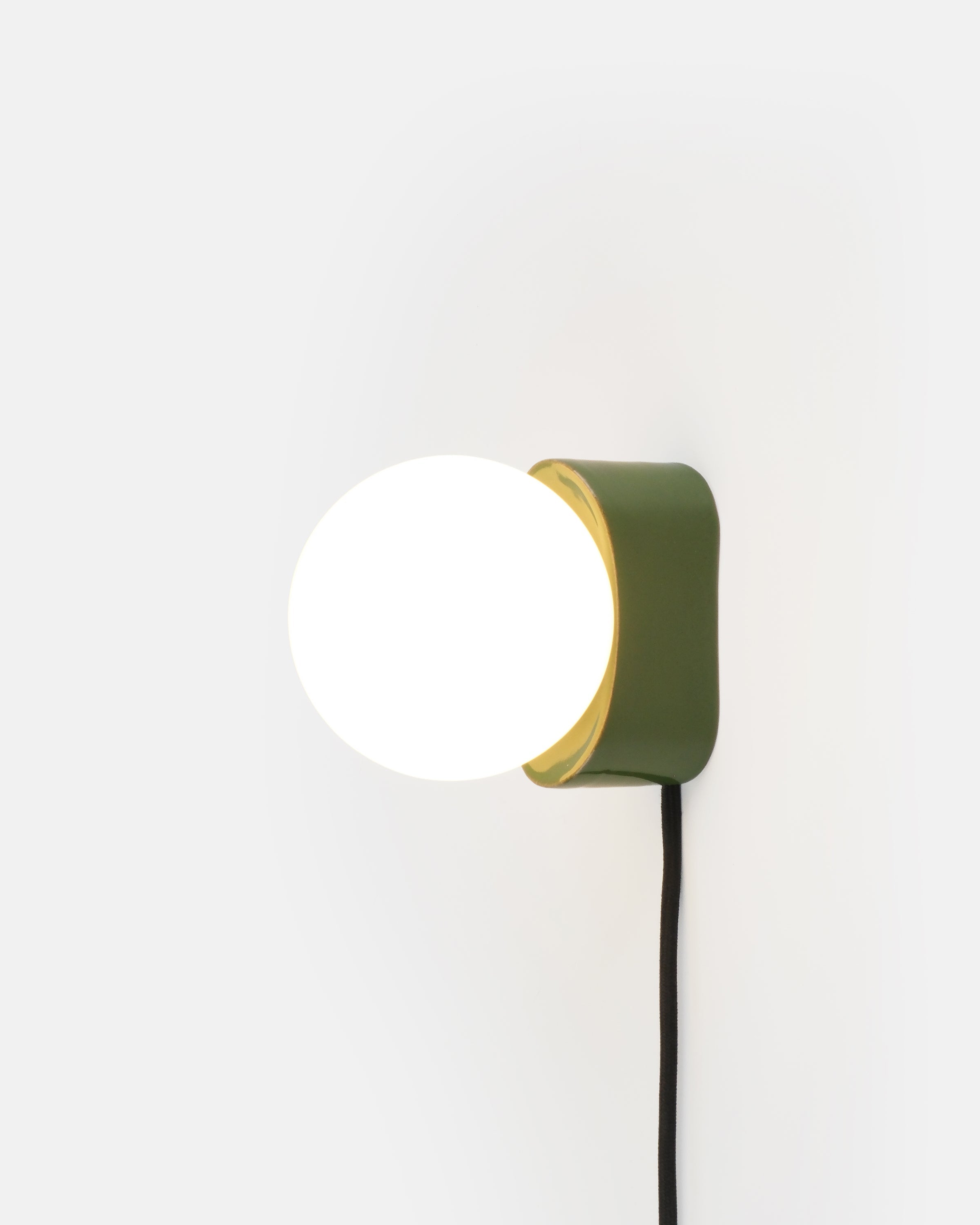 Iota Sconce wall lamp showing pill-shaped ceramic body and round glass globe in black glaze