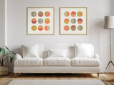 Two framed canvases each with a 3x4 grid of colorful half-circle shapes in warm sunset tones above a white three-seat sofa with cushions in a minimalist living room.