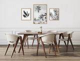 Dining room with dark wood table and six cream upholstered chairs, featuring three black and white palm tree and leaf prints in light wooden frames on a white wall.
