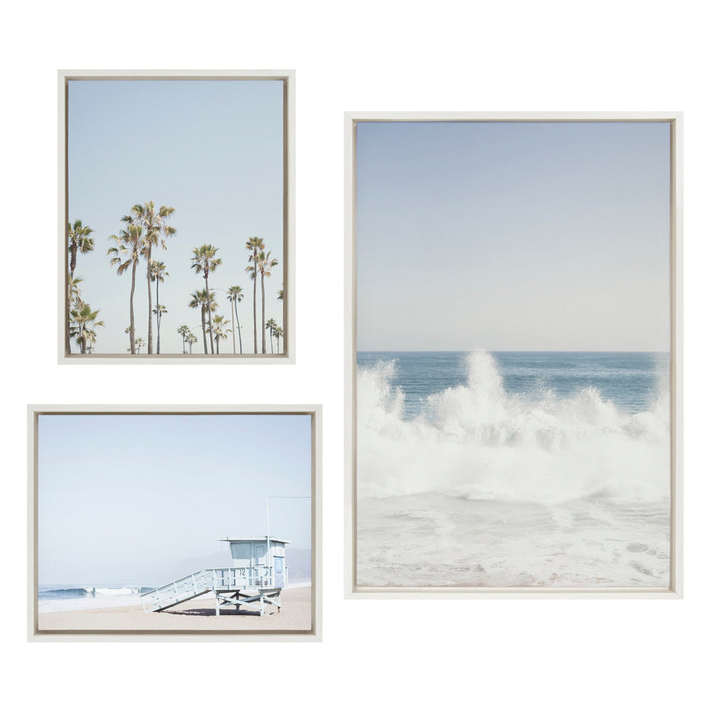 Three framed canvases showing coastal scenes: tall palm trees against a clear sky, a lifeguard tower on a sandy beach, and large ocean waves crashing with white foam under a pale blue sky.