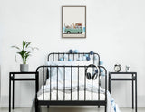 Children's bedroom with black metal bedframe draped in blue and white ball string lights, flanked by black side tables and a framed canvas of animals in a turquoise van above.