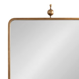 Rectangular mirror with rounded corners and a thin brass-colored metal frame topped by a decorative finial featuring a small sphere and rod
