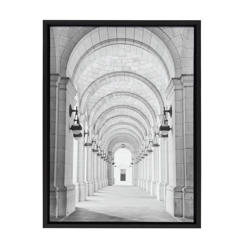 Black and white photograph of a long, vaulted corridor with repeating arches and wall-mounted lanterns, framed in a simple black frame.