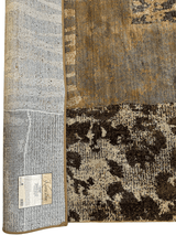 Close-up of a Karastan Carmel Santa Lucia Chestnut Area Rug showing a textured mix of brown, beige, and gray tones with an abstract pattern and a label on the rug's reverse side.