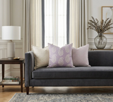 Three decorative pillows on a dark gray sofa, featuring a lilac paisley patterned pillow in the center flanked by a solid beige and a pink pillow with a subtle geometric design.